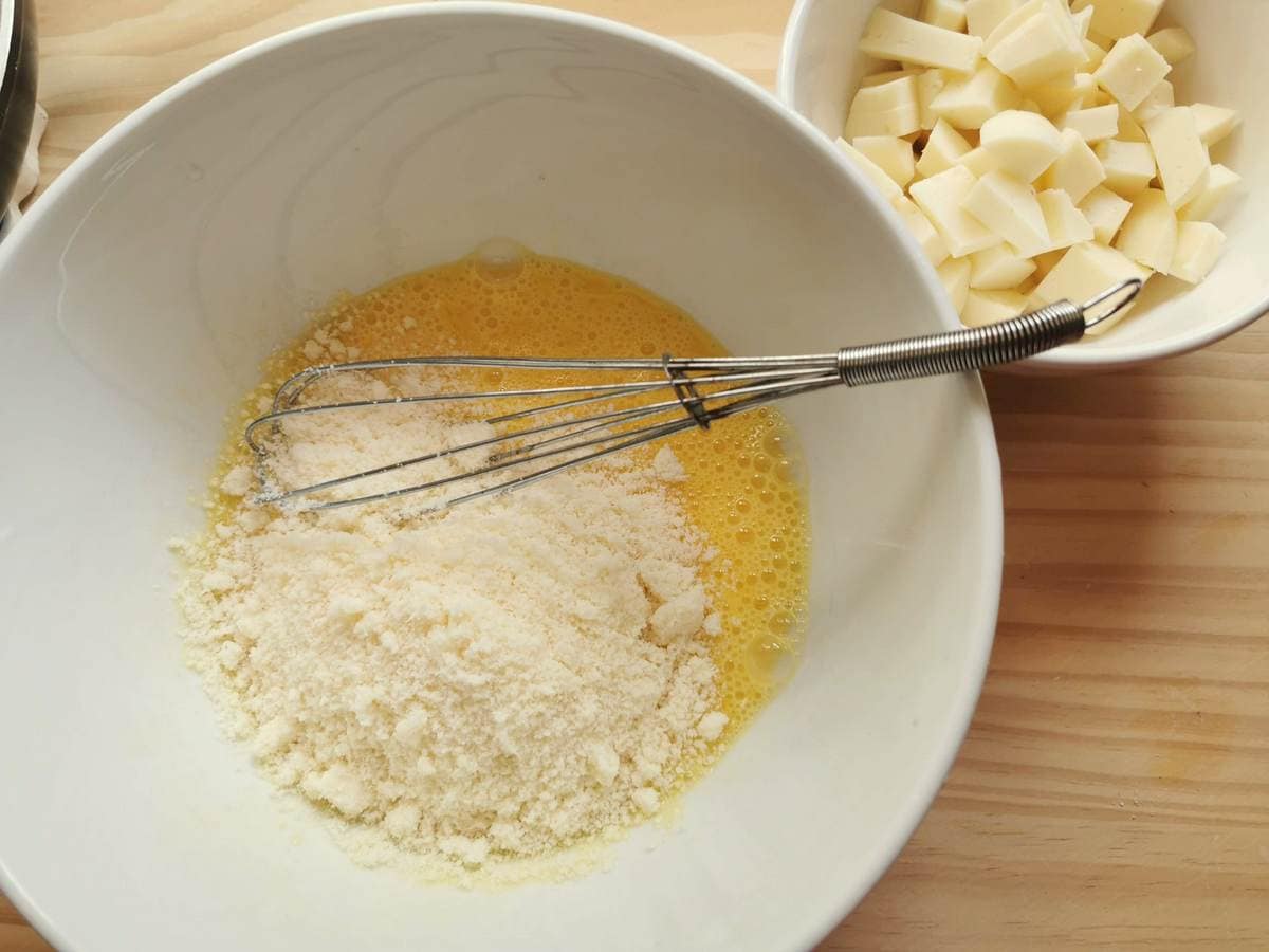 Grated parmigiano cheese in white bowl with beaten eggs.