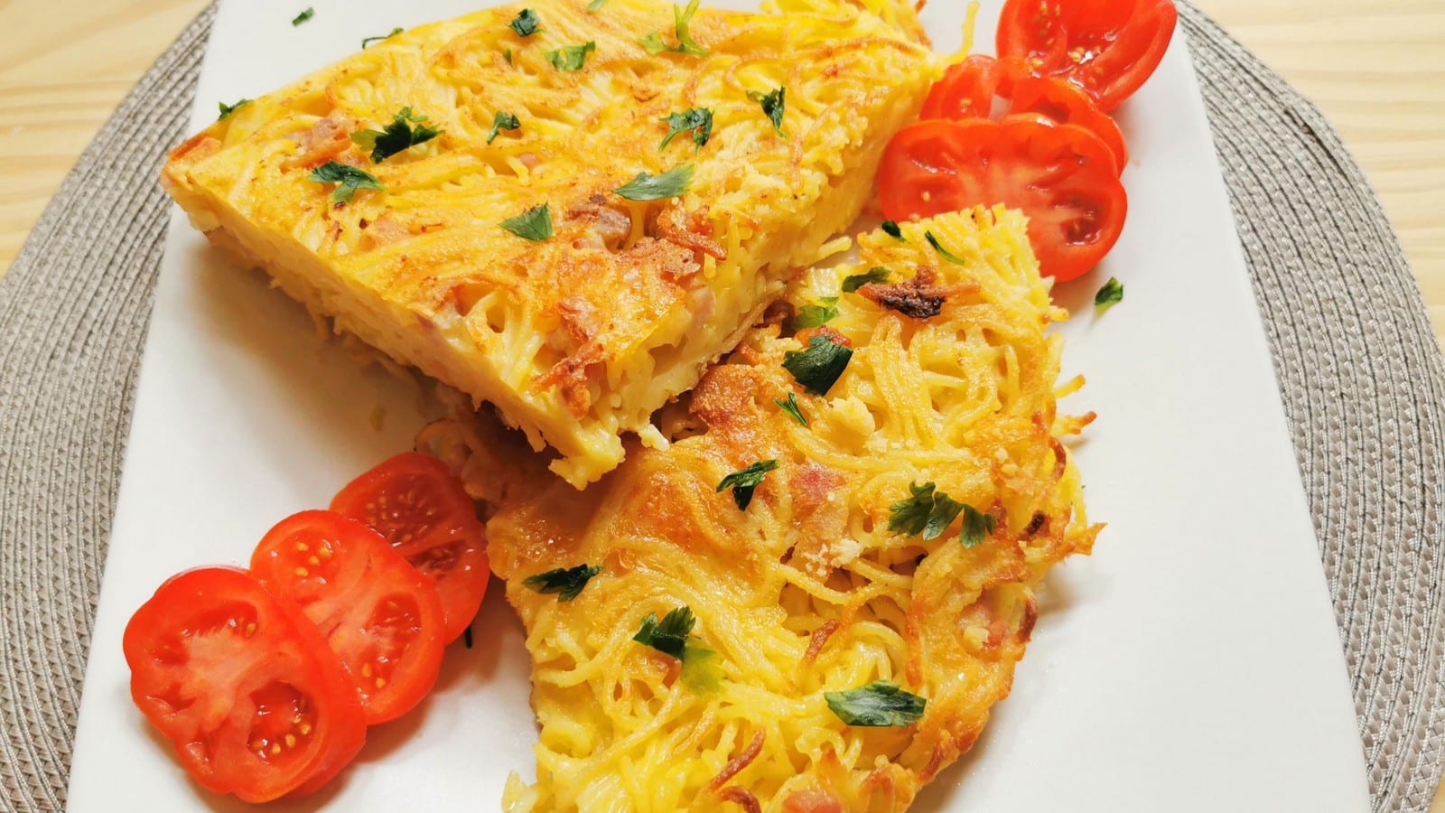 Slices of spaghetti frittata on white plate with tomato slices.