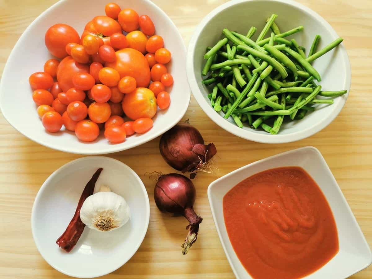 Ingredients for green bean pasta sauce in white bowls on wood board.