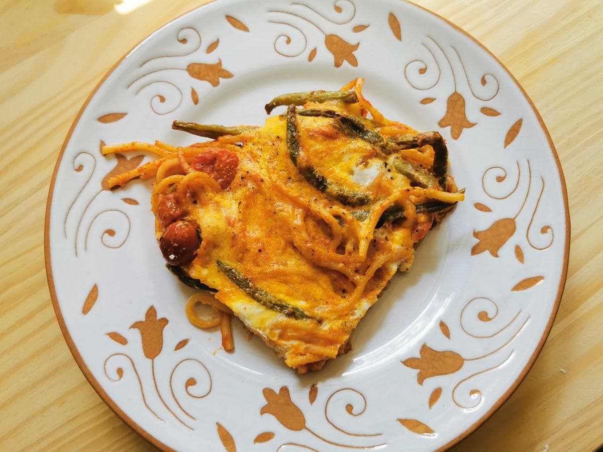 A slice of frittata made with leftover spaghetti with green beans on a white plate.