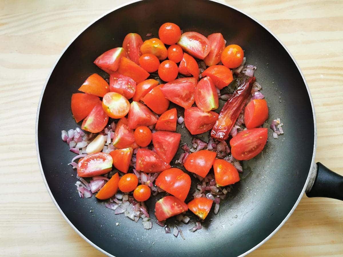 Tomato pieces in skillet with onions, garlic and chilli pepper (peperoncino).