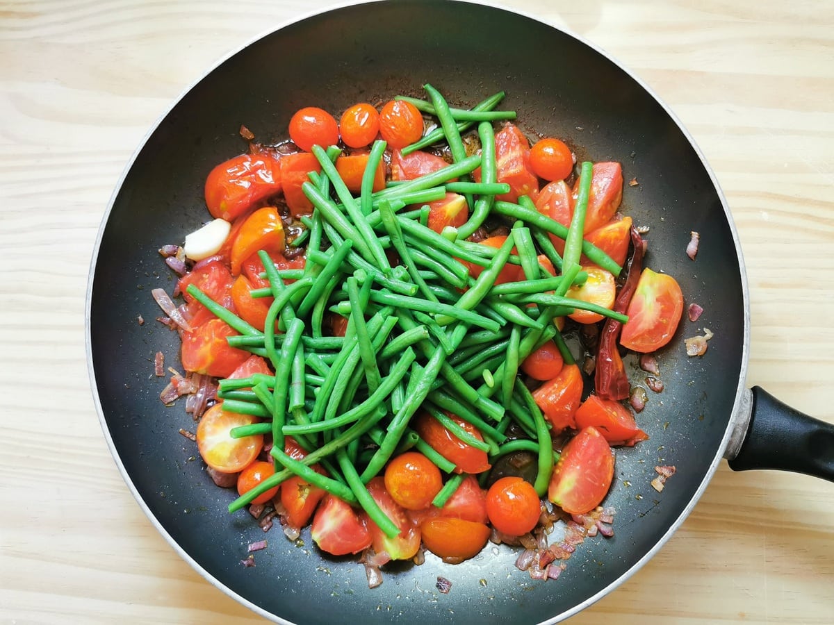 Blanched green beans in skillet with tomatoes, onions and garlic.