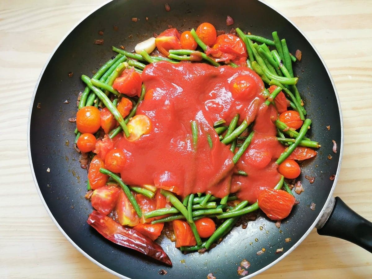 tomato passata added to skillet with green beans and tomatoes.