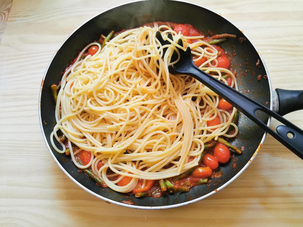 Cooked spaghetti in skillet with green bean and tomato sauce.