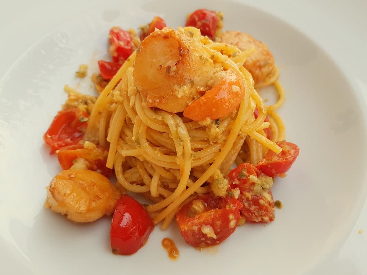 Spaghetti with scallops, citrus fruit and cherry tomatoes on a plate.