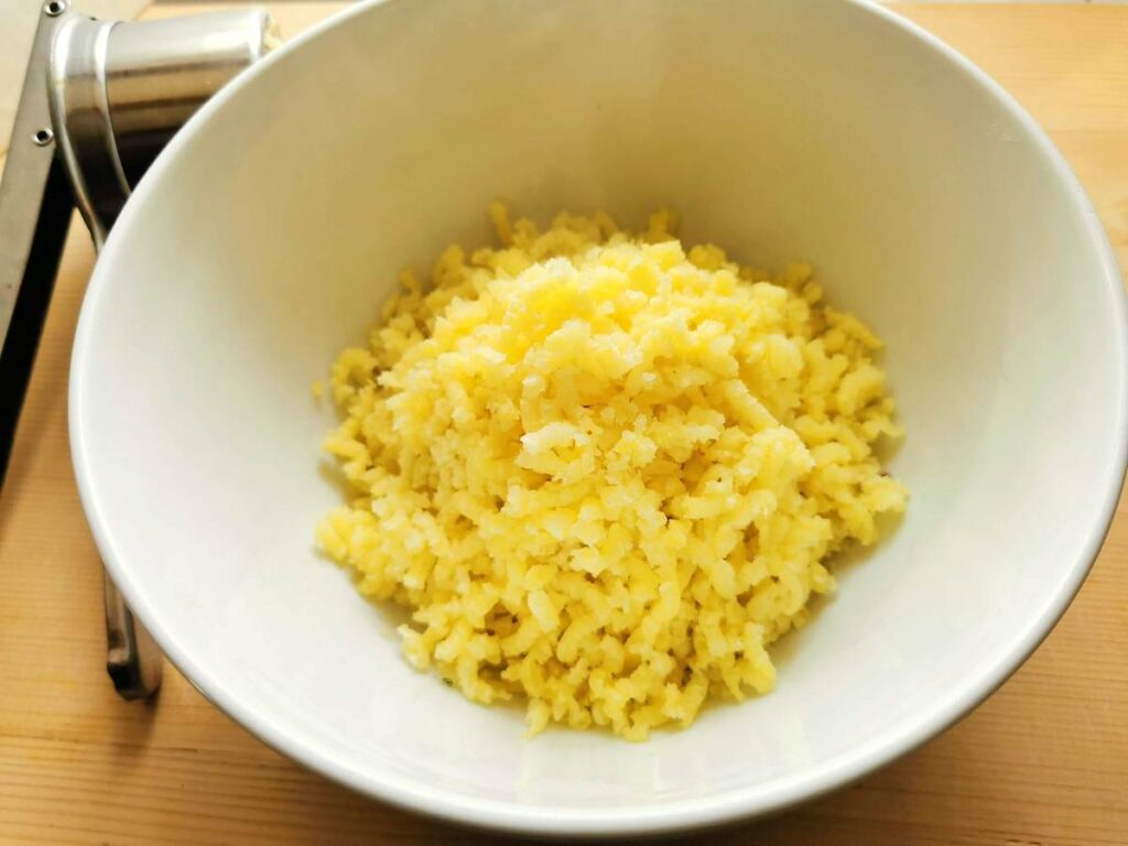 cooked and peeled potato passed through a ricer in white bowl.