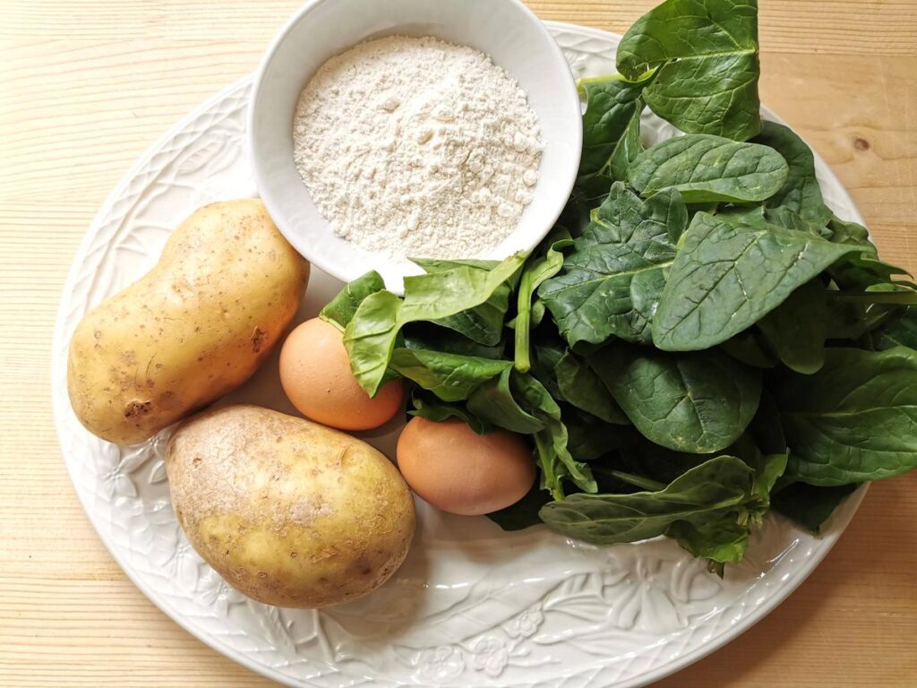 ingredients for spinach and potato gnocchi on white plate.