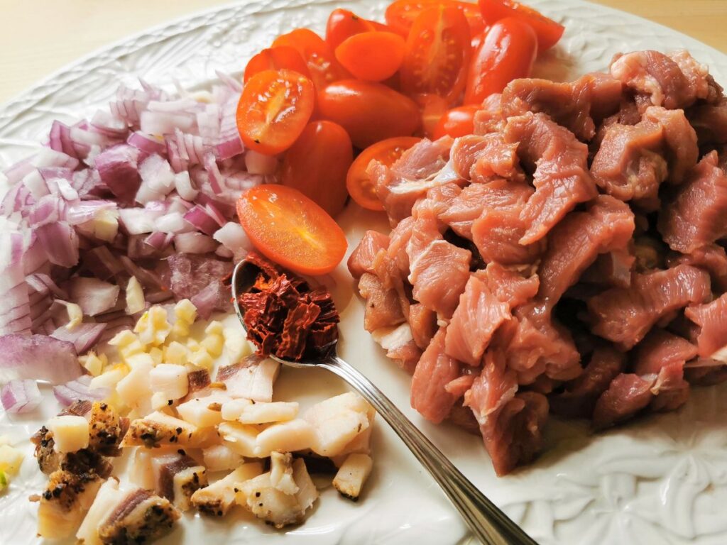 ingredients for lamb ragu prepared for cooking on white plate.