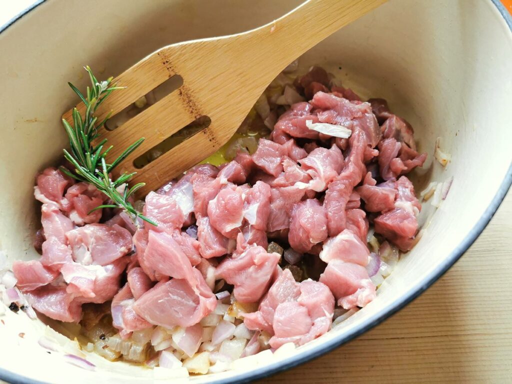 uncooked lamb pieces and sprig of rosemary added to Dutch oven