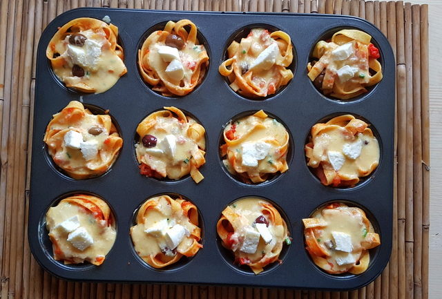 tagliatelle pasta muffin nests in muffin tin with cubed mozzarella on top