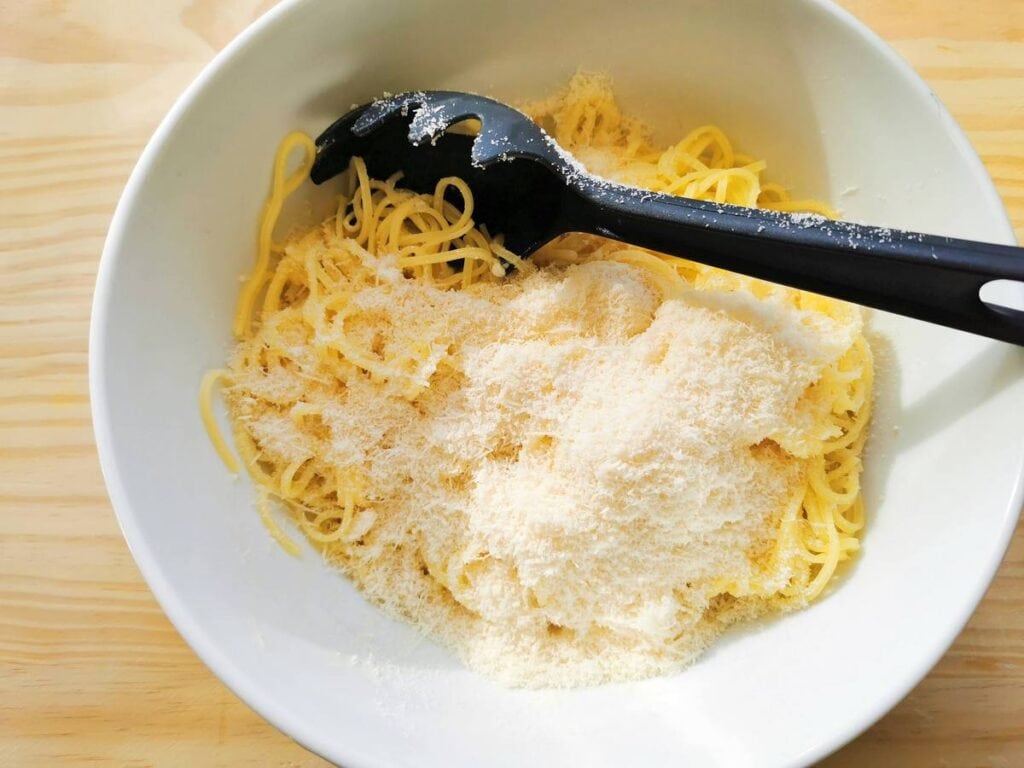 grated cheese added to cooked spaghetti in white bowl