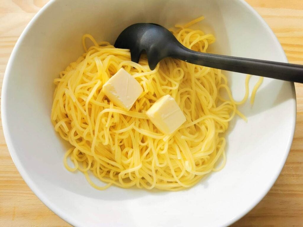 cooked spaghetti in white bowl with pieces of butter