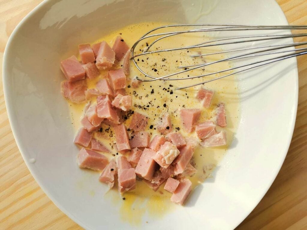 chopped ham in white bowl with beaten egg yolks and cream