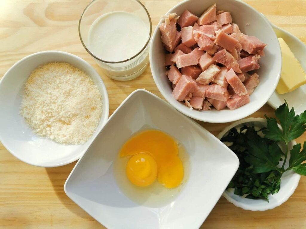 chopped ham in white bowl, egg yolks in white bowl, grated cheese in white bowl and chopped parsley