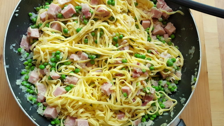 cooked tagliolini, ham, pancetta, peas and onions in frying pan