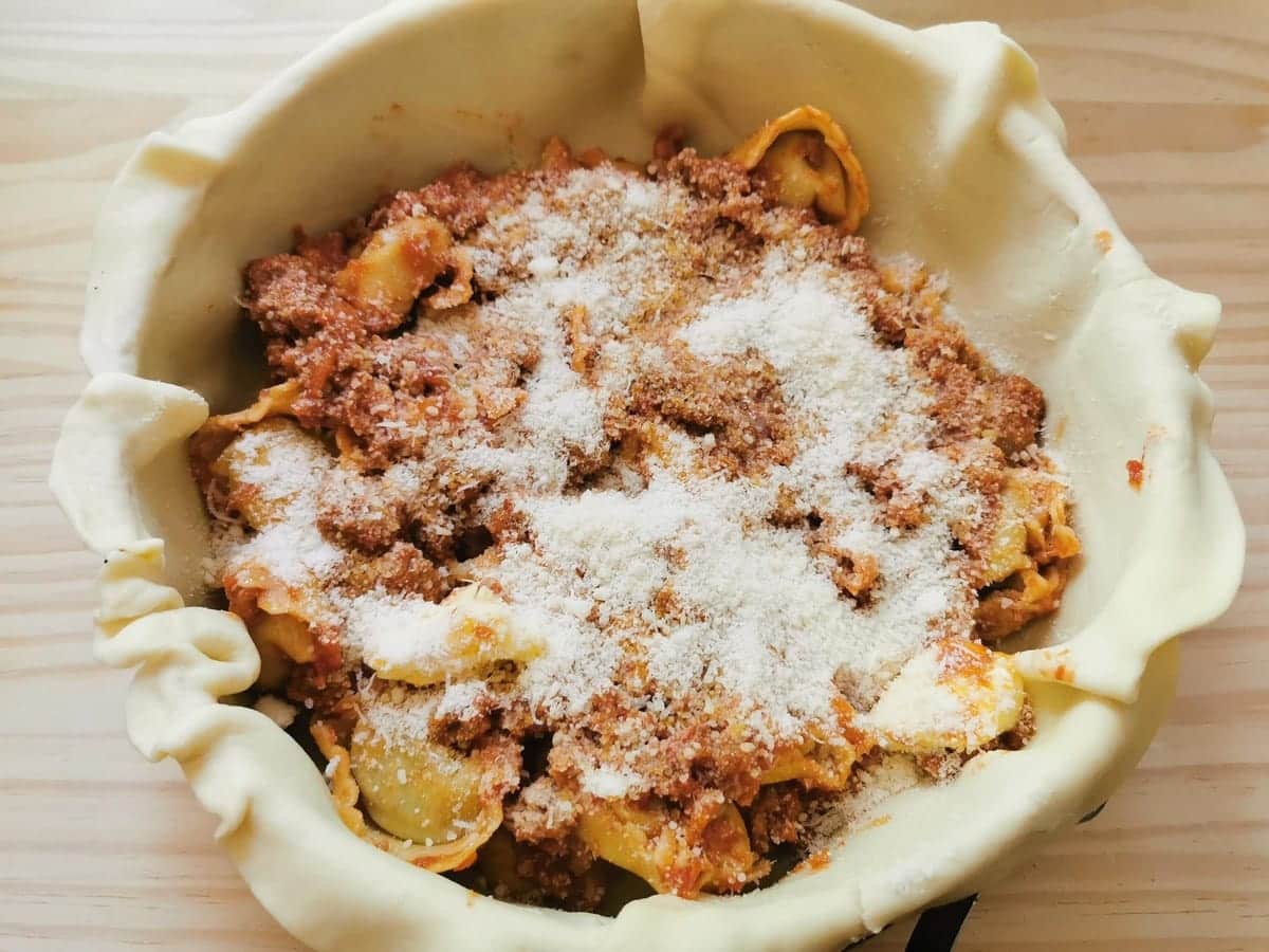 Bolognese sauce and grated Parmigiano layered on top of tortellini in cake tin.