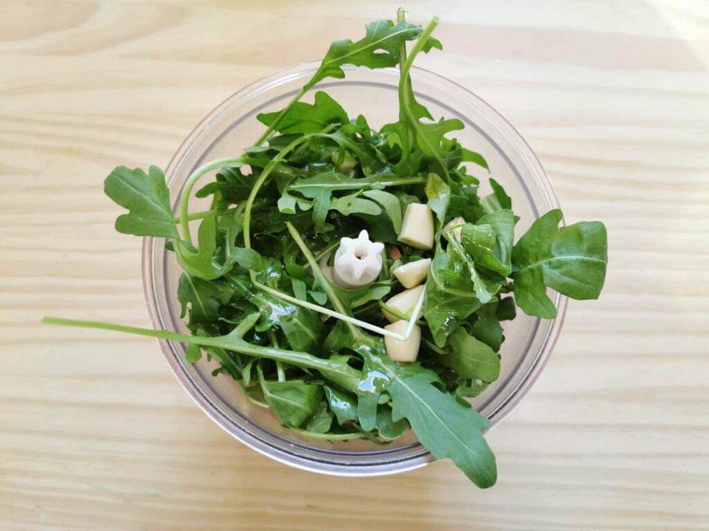 feuilles de roquette (roquette) et gousses d'ail dans un robot culinaire