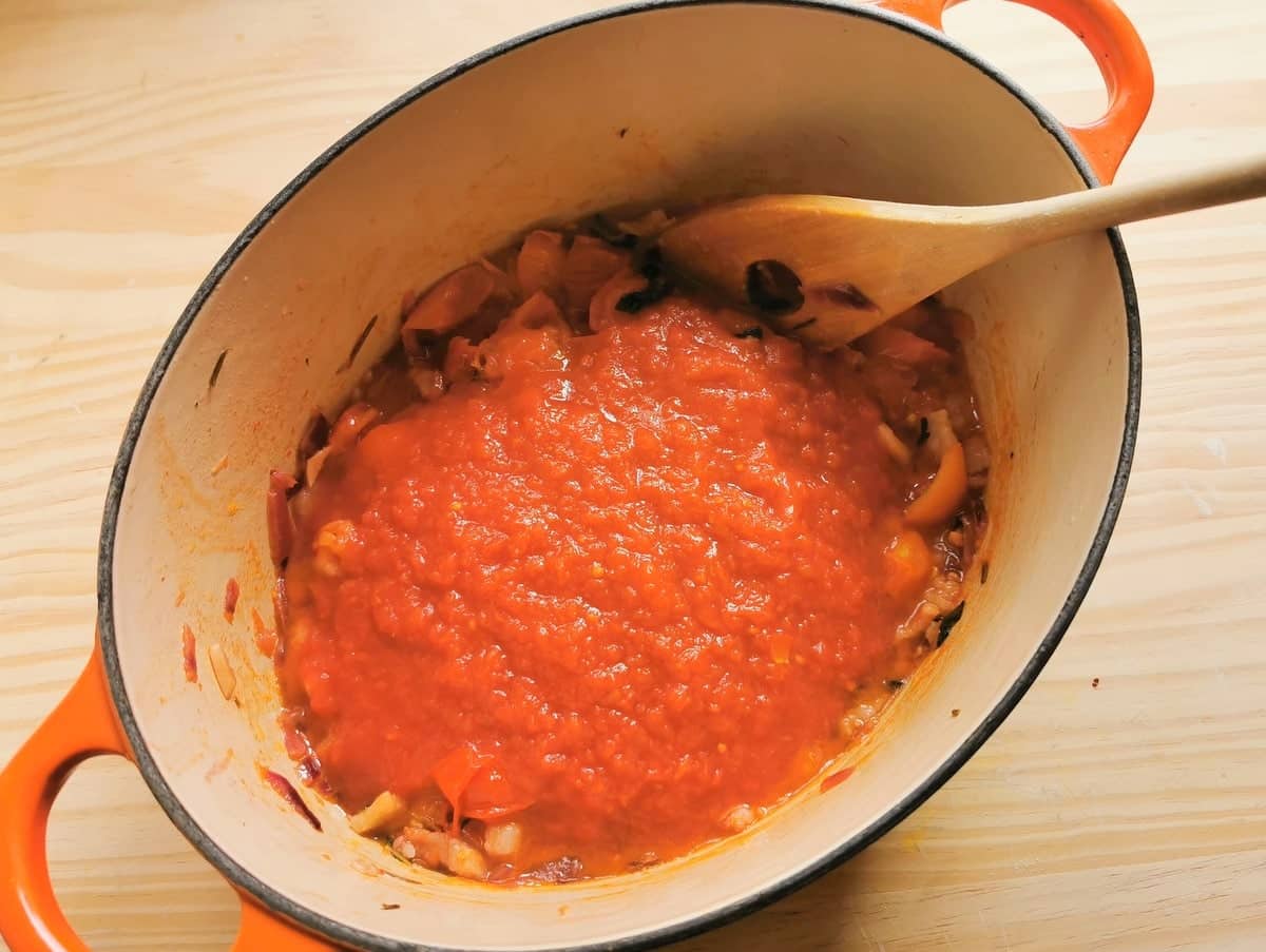 Tomato passata added to Dutch oven with tomatoes, onions amd lardo