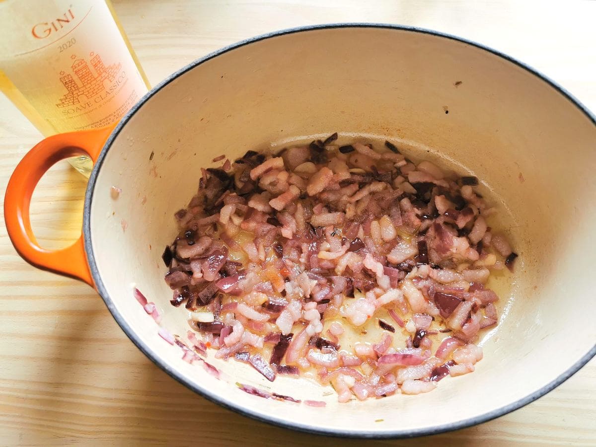 Cooked onions and lardo in Dutch oven next to bottle of white wine