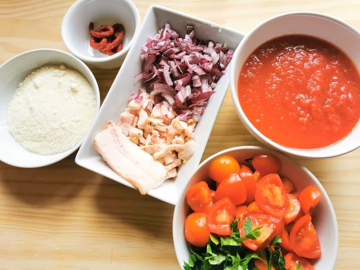Chopped onions and lardo in white bowl. Chopped tomatoes and parsley in second white bowl and tomato passata, tomato concentrate and grated cheese in white bowls